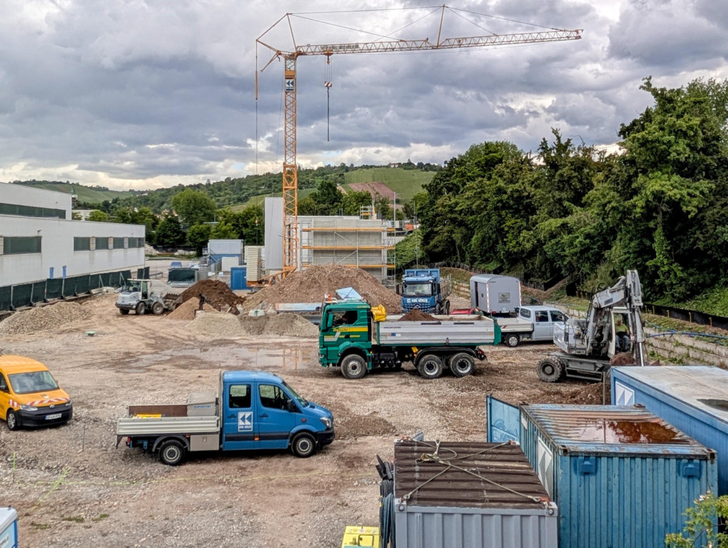 Baustelle des Green Hydrogen Hub im Stuttgarter Hafen mit Baukran, Erdhaufen, Lkw und Baucontainern vor grünen Hügeln
