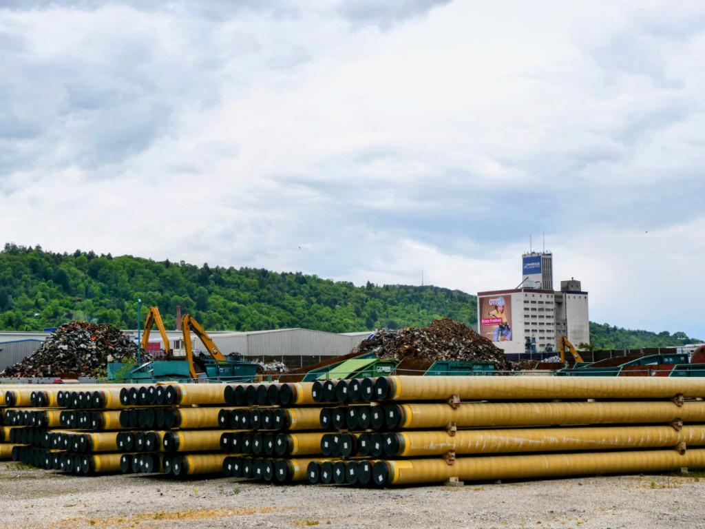 Gestapelte gelbe Wasserstoffpipeline-Rohre auf einem Lagerplatz im Stuttgarter Hafen, im Hintergrund Schrottberge und Industriegebäude