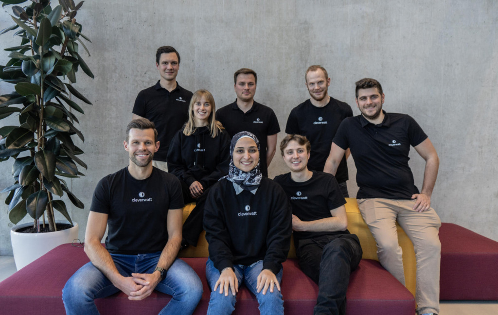 Gruppenfoto des cleverwatt-Teams: Acht Personen in schwarzen cleverwatt-Shirts posieren lächelnd in einem modernen Büro