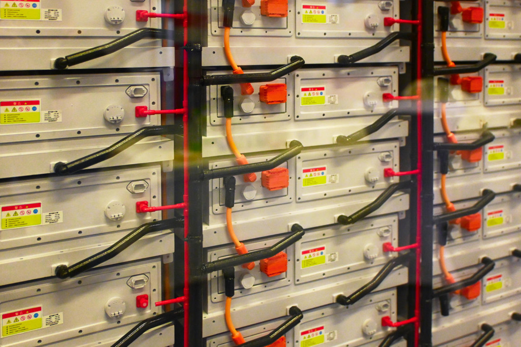Nahaufnahme aneinandergereihter Batteriemodule eines Großspeichers mit orangefarbenen und roten Anschlusskabeln