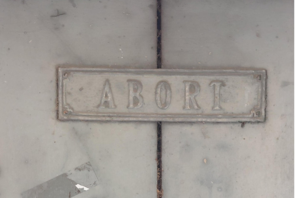 Altes Emailleschild mit der Aufschrift 'Abort' an einer Steinwand – Sinnbild für die kritisierte Energiepolitik von Ministerin Reiche
