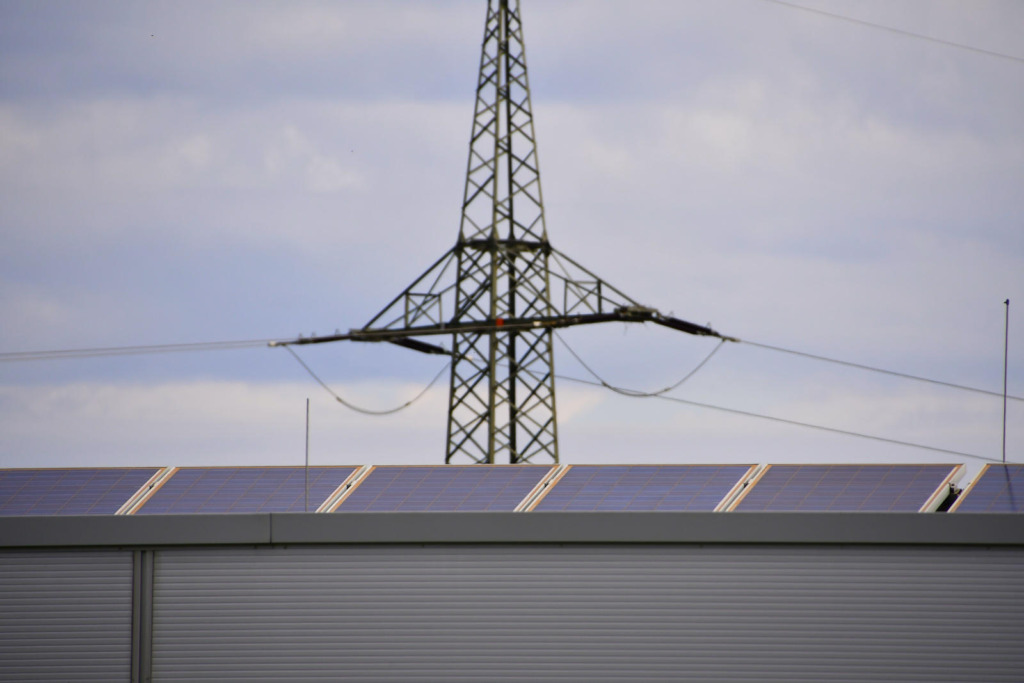 PV-Dachanlage auf Gewerbehalle im Vordergrund, im Hintergrund ein Hochspannungsmast