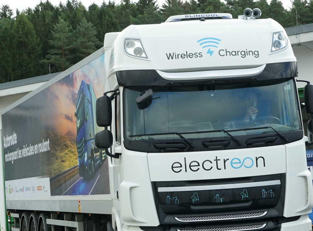 Weißer LKW mit Fahrerhaus-Aufschrift „Wireless Charging" und Electreon-Logo, im Hintergrund ein Auflieger mit französischsprachigem Werbemotiv zu induktivem Laden auf der Autobahn.