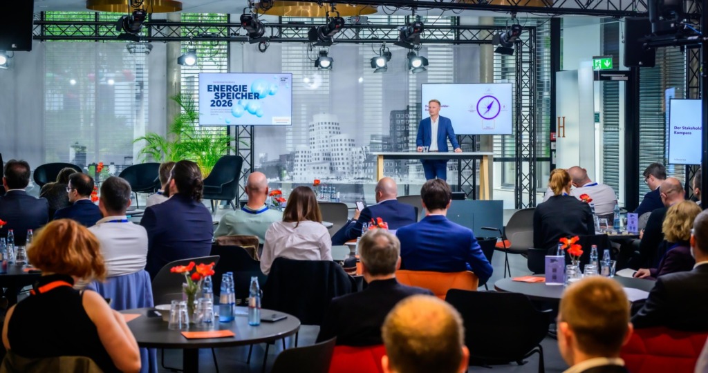 Publikum an Bistrotischen verfolgt einen Vortrag auf der Konferenz „Energiespeicher 2026“ des Handelsblatts in Düsseldorf; links ein Bildschirm mit dem Konferenztitel