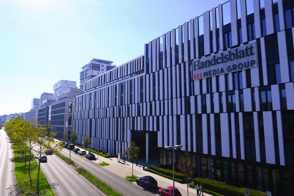 Moderne Bürofassade mit weißen Lamellen und dem Schriftzug „Handelsblatt Media Group“ an einer baumgesäumten Straße in Düsseldorf