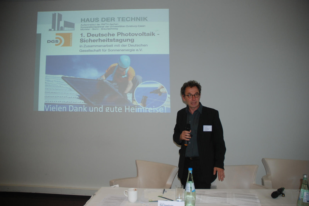 Ralf Haselhuhn spricht bei der 1. Deutschen Photovoltaik-Sicherheitstagung von Haus der Technik und DGS. Hinter ihm ist die Abschlussfolie zu sehen.