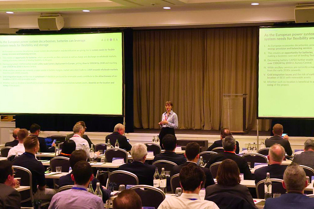 Konferenz zu C&I-Batteriespeichern in Frankfurt: Referentin vor zwei Leinwänden mit Folien von Aurora Energy Research, im Vordergrund das Publikum an Tischreihen