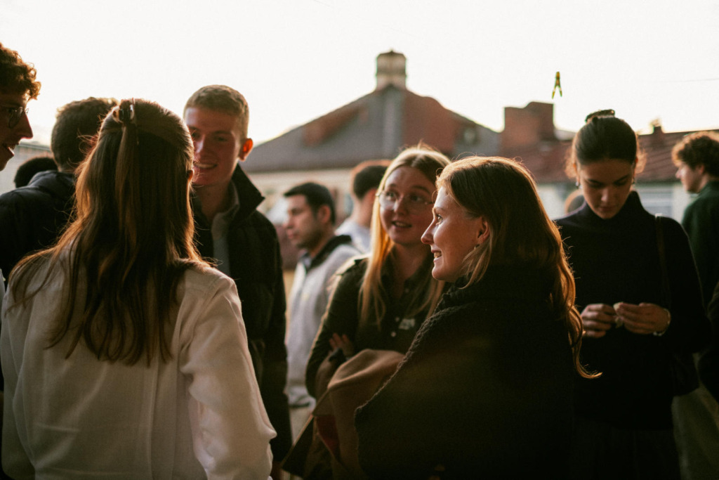 Junge Menschen stehen im warmen Abendlicht auf einer Dachterrasse in München und unterhalten sich, im Hintergrund Hausdächer.